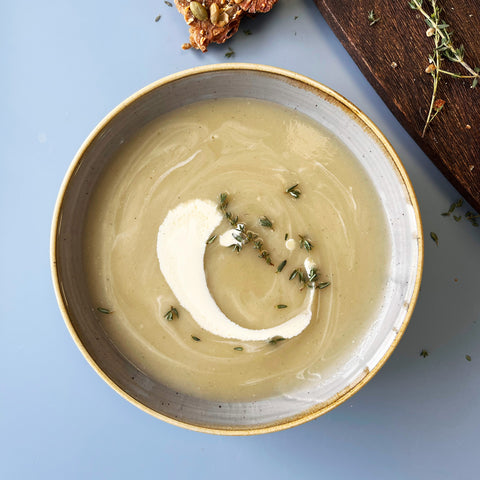Bowl of soup with a swirl of cream and herbs on a blue background